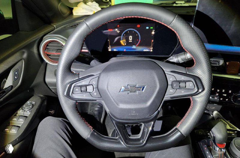 Рулевое колесо и панель приборов Chevrolet Trax крупным планом, видно шильдик Chevy на руле и цифровой щиток приборов.