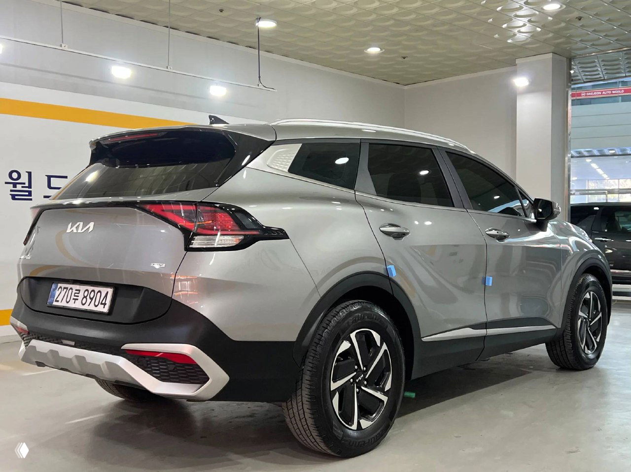 KIA Sportage 2023 вид сзади и в профиль в автосалоне, чётко видна задняя оптика, бампер и окраска кузова, автомобиль на колёсах.