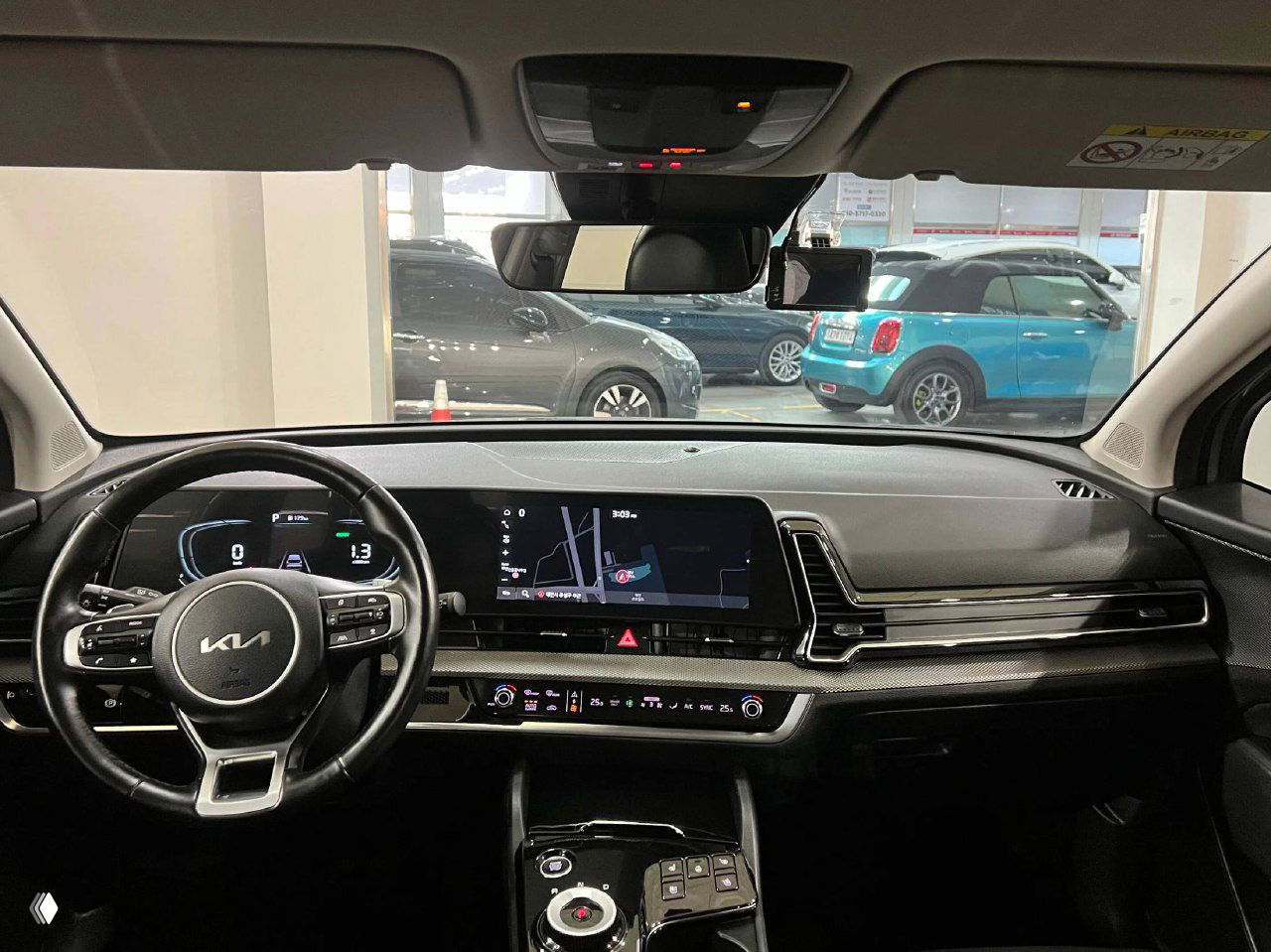 Панорамный вид на приборную панель и мультимедийный экран KIA Sportage 2023, рулевое колесо с логотипом KIA и цифровая комбинация приборов.