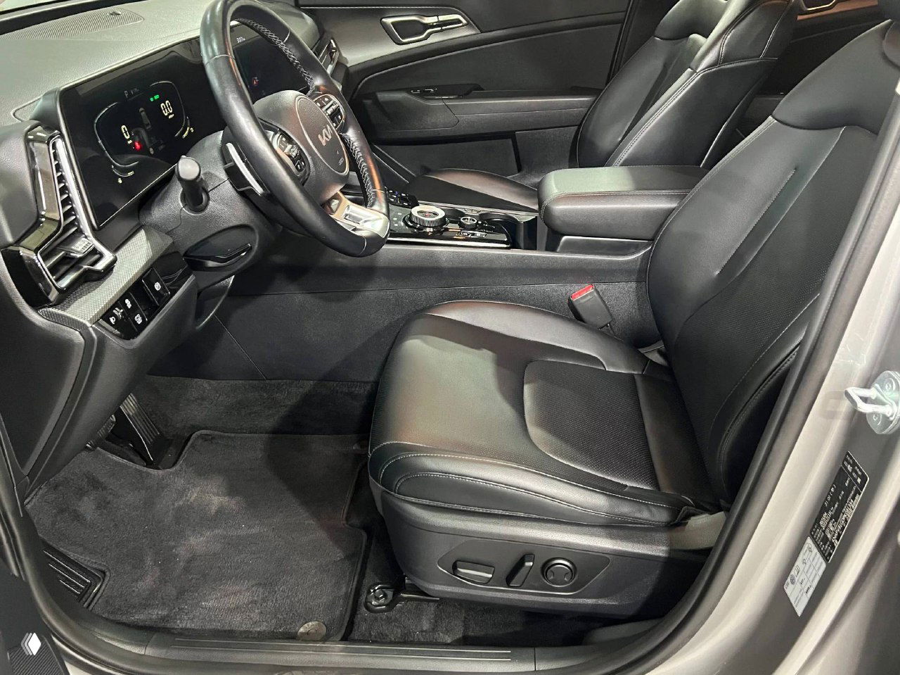 Водительское место и передние сиденья KIA Sportage 2023: кожаная обивка, регулировки сиденья и общий вид салона со стороны дверного проёма.