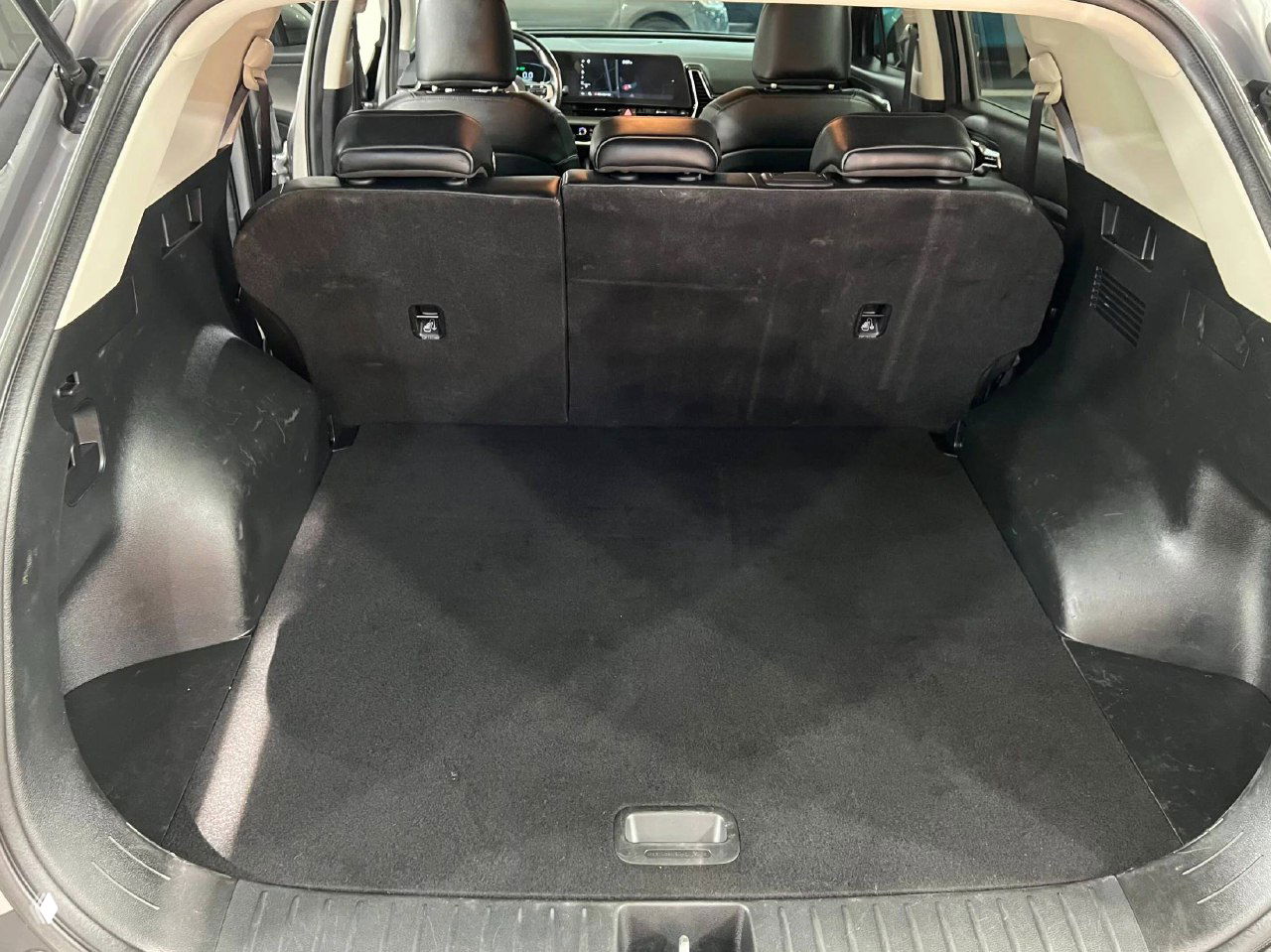 Багажное отделение KIA Sportage 2023 с опущенными задними сиденьями, чистый коврик багажника и вид на заднюю часть салона из багажника.