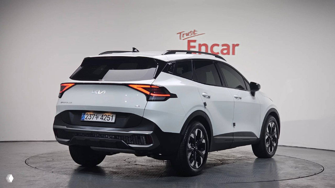 Задний ракурс белого KIA Sportage 2024 на поворотном подиуме, видна задняя оптика и корейская номерная табличка, автомобиль без посторонних людей в кадре.