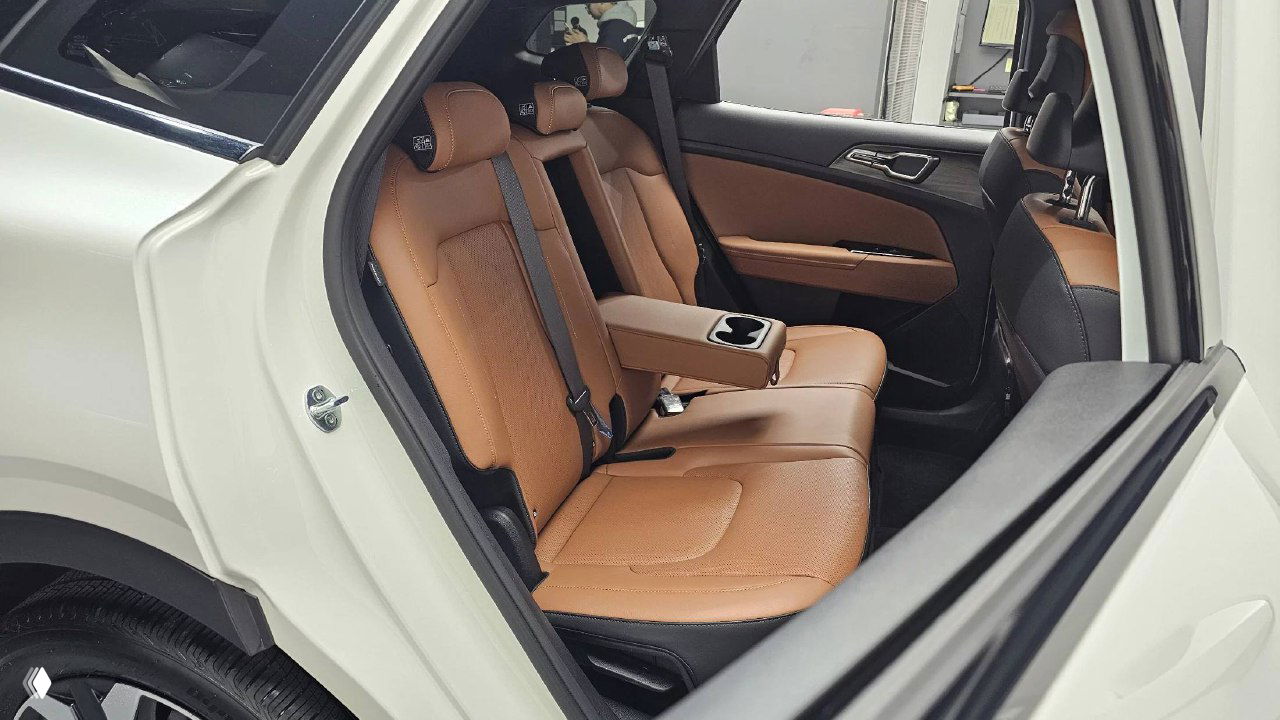 Задние пассажирские сиденья KIA Sportage 2024 с опущенным подлокотником, коричневая кожа, три посадочных места и подстаканники в центре.