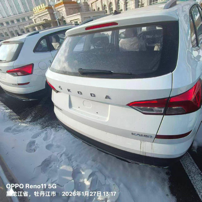 Задняя часть белой Skoda Kamiq 2025 года на парковке; пустой номерной знак, видна надпись SKODA и детали багажника, зимний фон.