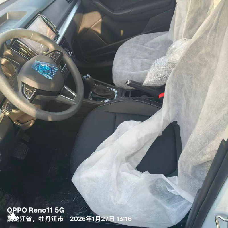 Интерьер Skoda Kamiq: вид на переднее сиденье и руль, защитные белые чехлы на сидениях, коробка передач и элементы торпеды.