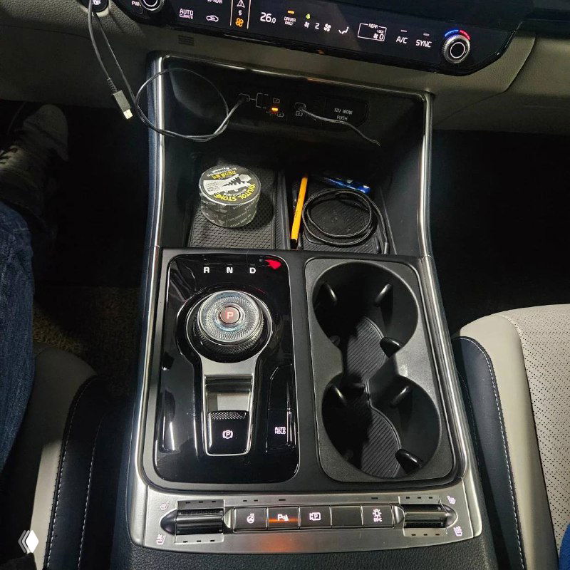 Ближайший план центрального тоннеля KIA Carnival с селектором передач, подстаканниками и органайзером в нише между сиденьями.