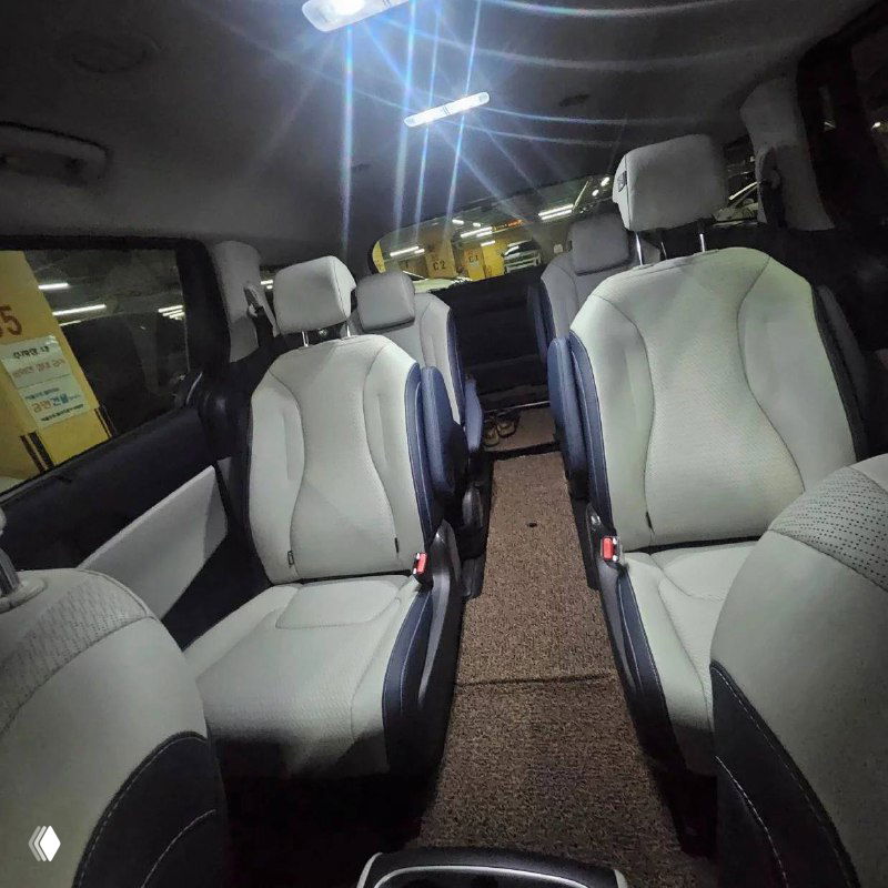 Третий ряд сидений KIA Carnival с тремя посадочными местами в светлой обивке, видна общая компоновка салона и напольные коврики.