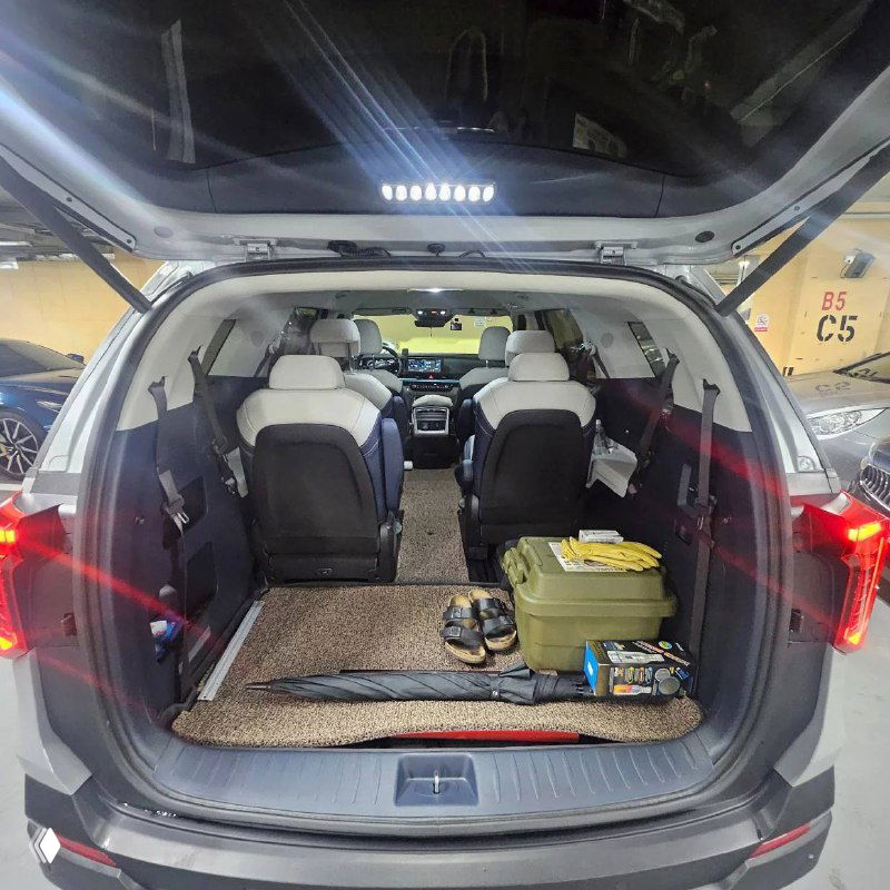 Открытый багажник KIA Carnival с багажом и предметами, видна глубина грузового отсека и доступ к третьему ряду сидений.