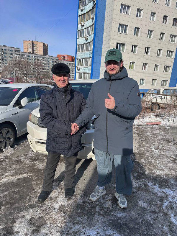 Два человека на парковке рядом с белым Honda Crossroad, один показывает жест «палец вверх»; фотография во время передачи автомобиля клиенту.