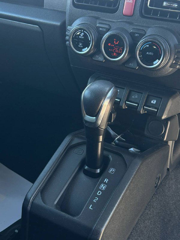 Селектор коробки передач Suzuki Jimny — крупный план рычага АКП, центральный туннель и клавиши дополнительных функций на консоли, отчётливо видно подписи передач.