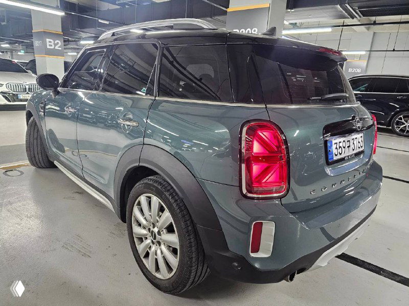 Вид сзади Mini Cooper Countryman 2022 в паркинге: задние фонари, багажник и форма кузова, автомобиль на городской стоянке с соседними машинами.