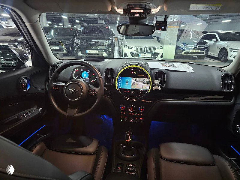 Фото салона Mini Cooper Countryman 2022: панель приборов, руль, центральная консоль с мультимедийным круглым дисплеем и подсветкой, чёрная отделка.