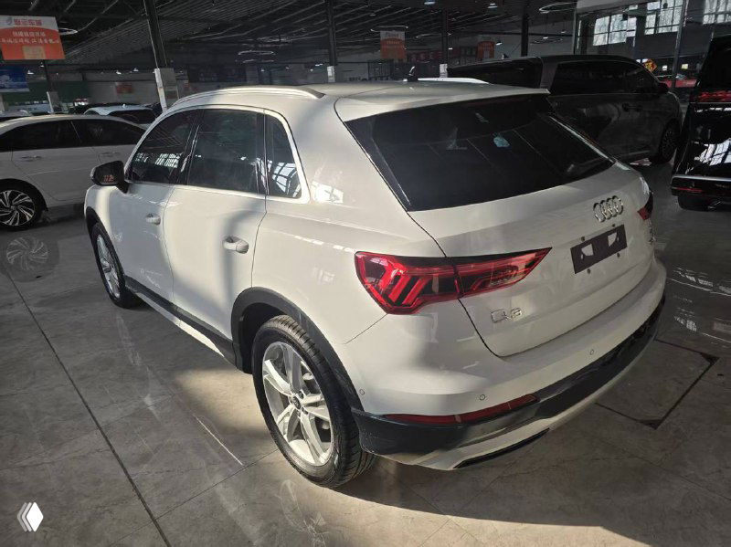 Вид сзади белого Audi Q3 2021 на стоянке, видно задние фонари, бампер и багажную дверь, автомобиль выставлен для продажи и осмотра покупателем.