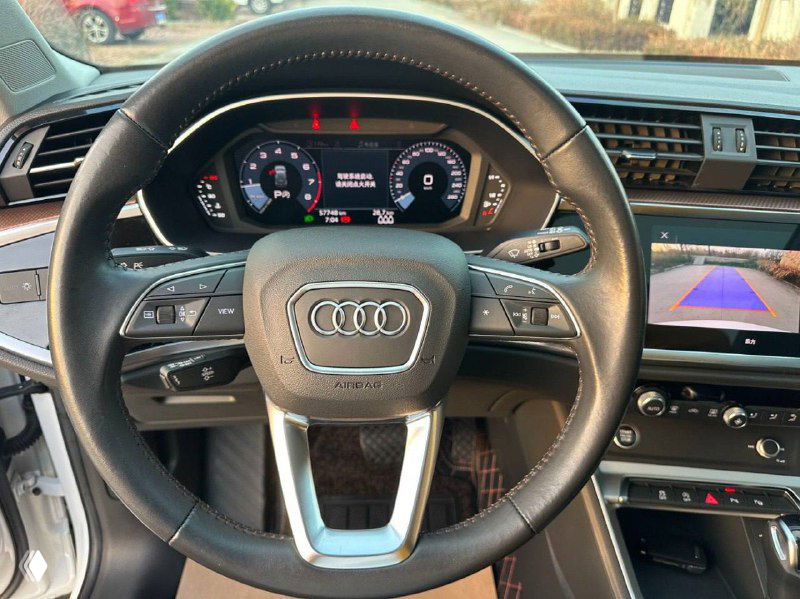 Салон: руль Audi Q3 крупным планом, приборная панель и мультируль, видны цифровая панель и элементы управления мультимедиа и круиз‑контроля.