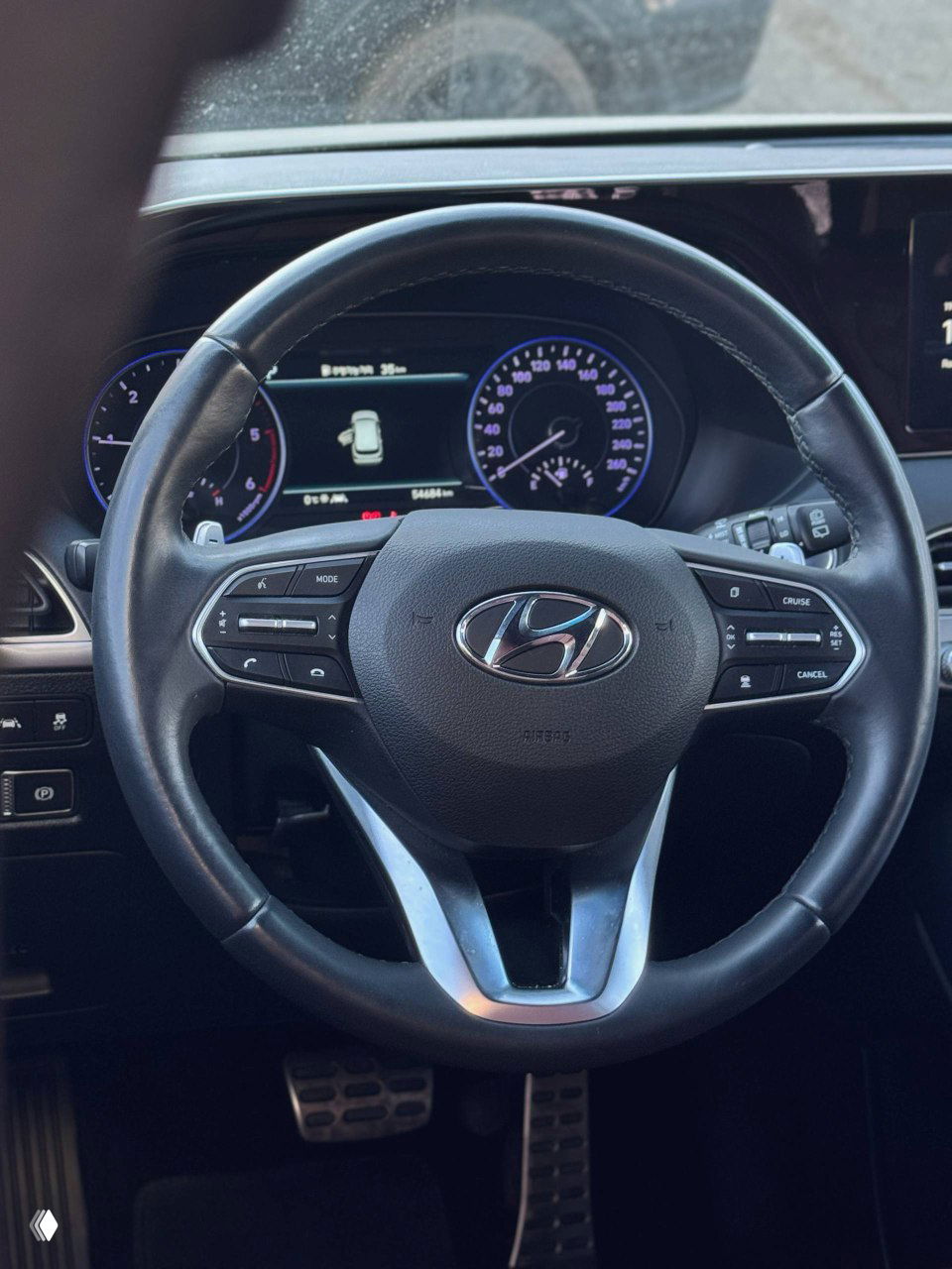 Крупный план рулевого колеса Hyundai с логотипом компании, элементы управления мультимедиа и приборная панель автомобиля с пробегом 54000 км.