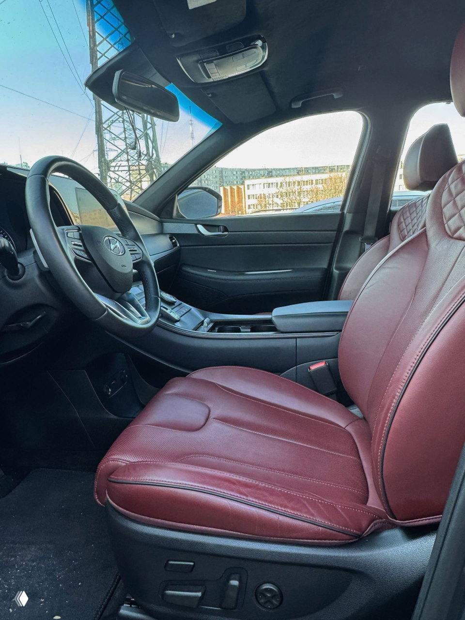 Вид на переднее сиденье водителя и панорамный обзор салона с бордовыми кожаными сиденьями и центральным подлокотником — аккуратный интерьер.