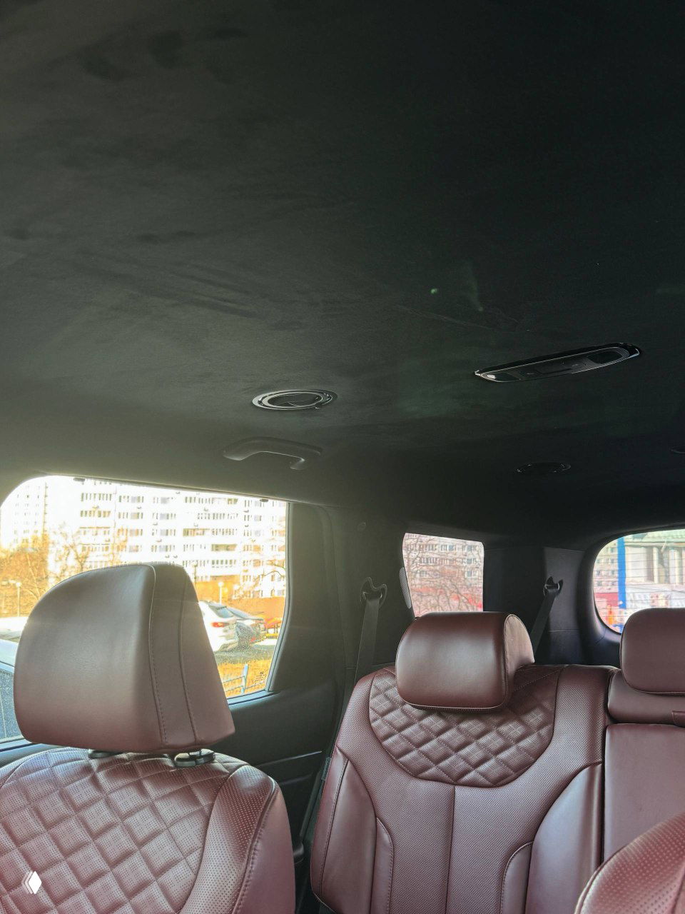 Вид вверх на потолок и верхнюю часть заднего ряда сидений с ромбовой прострочкой бордовой кожи и освещением потолка салона.