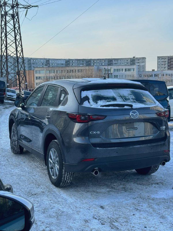Задний вид серой Mazda CX-5 2025 года на снежной парковке, открытая задняя часть багажника не видна, номер скрыт, фокус на кузове.