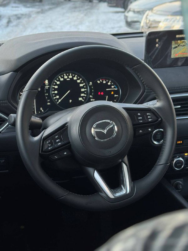 Руль и комбинация приборов Mazda CX-5 2025 в салоне: руль с кнопками, тахометр и спидометр, выглядит как минимум базовая комплектация.