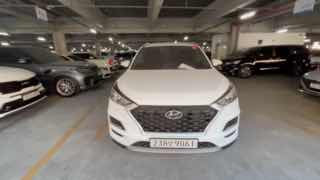 Фронтальный вид Hyundai Tucson в подземной парковке, показаны решётка радиатора, номерной знак и соседние автомобили на стоянке.