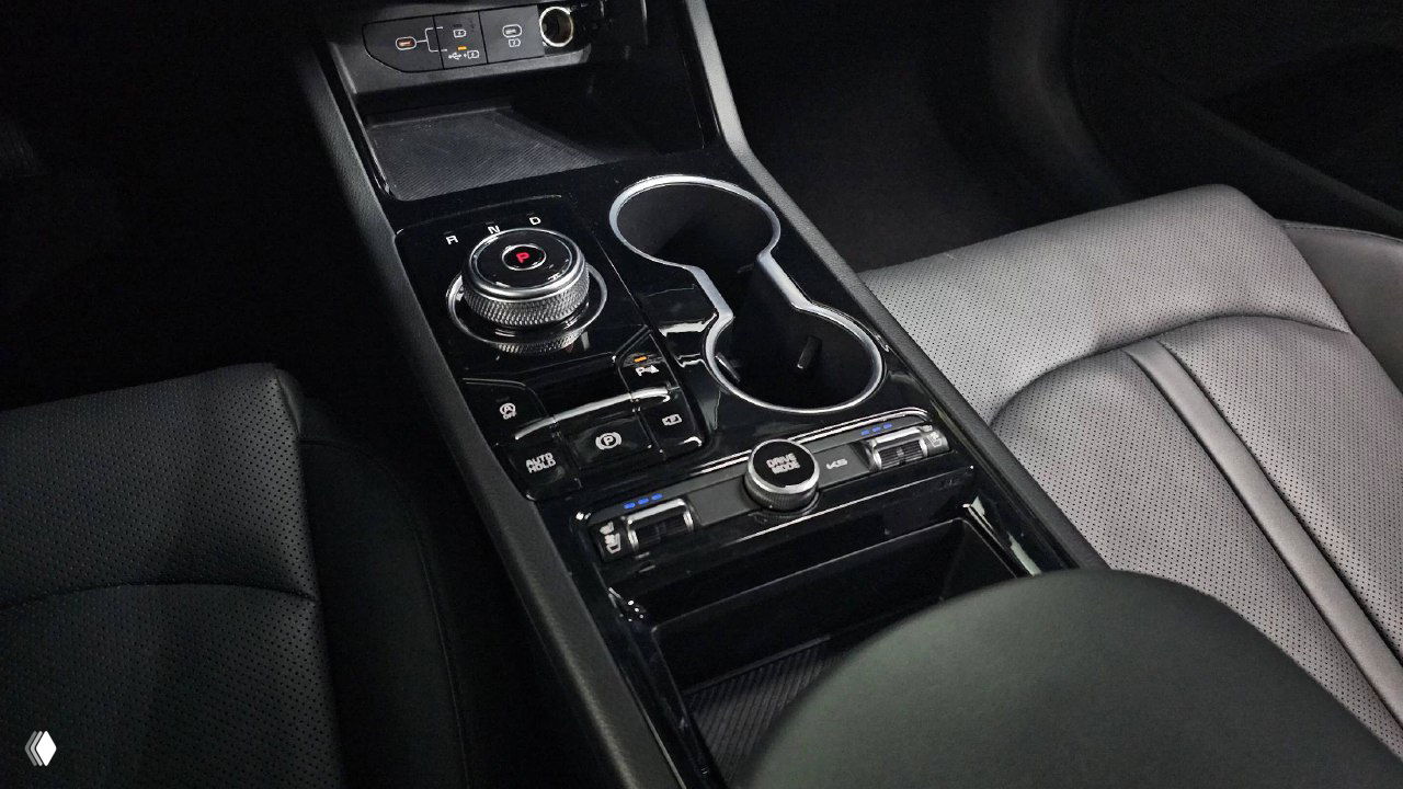 Центральный тоннель и селектор передач KIA K5 2024 — крупный план консоли, подстаканники и элементы управления в глянцевой отделке.