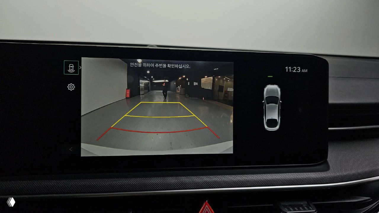 Экран мультимедиа KIA K5 2024 показывает изображение с камеры заднего вида и разметку парковки — демонстрация ассистентов и систем помощи.