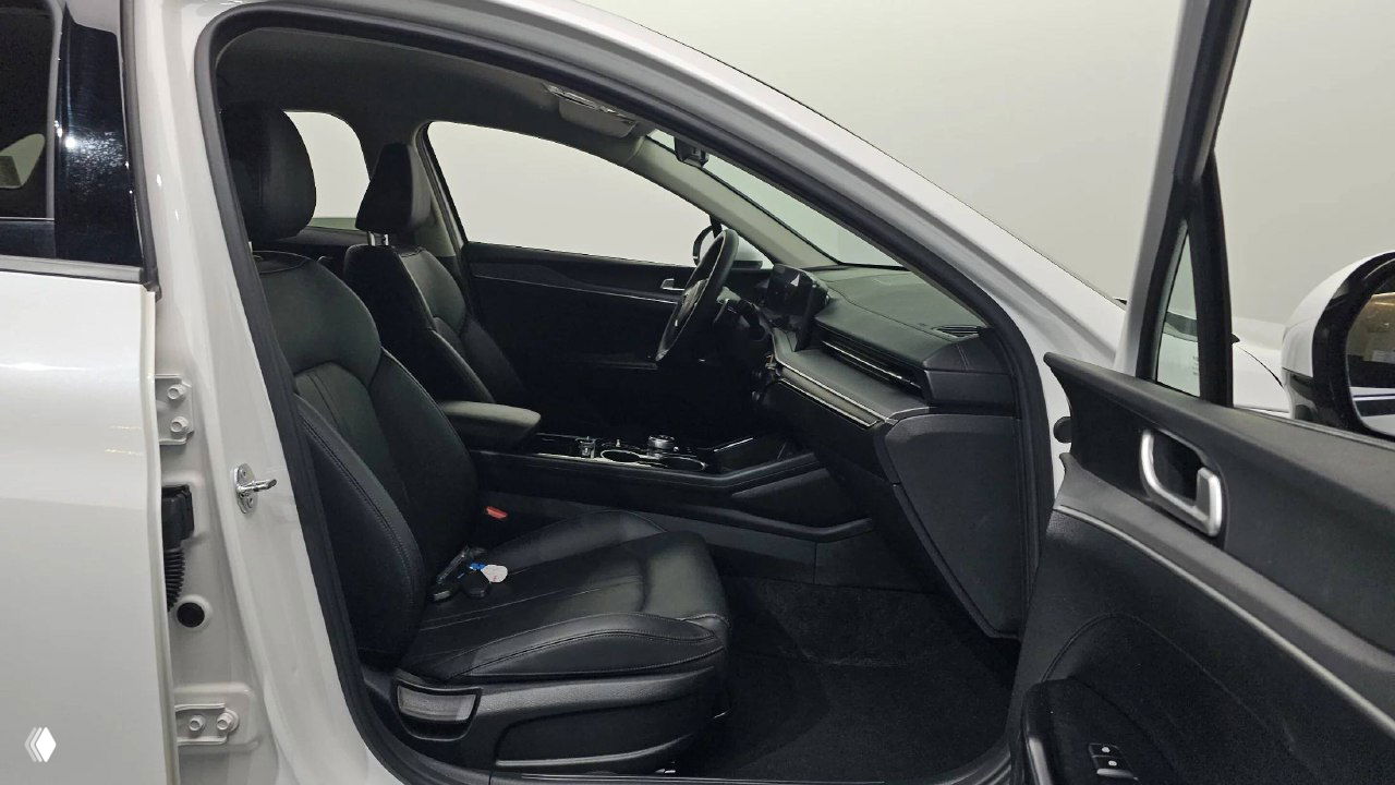 Водительское место и переднее кресло KIA K5 2024: открытая дверь, чёрные сиденья, вид на подлокотник и панель управления возле двери.