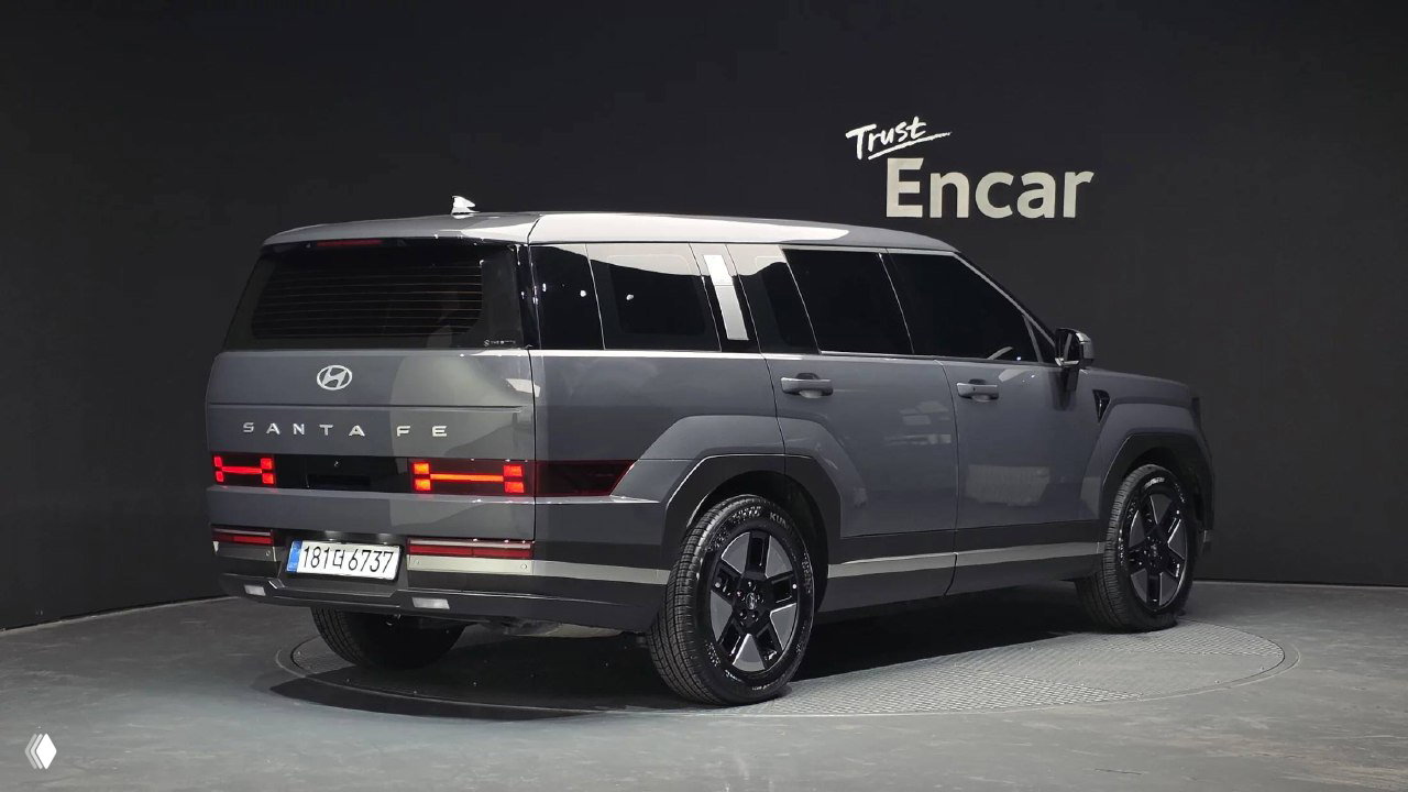 Hyundai Santa Fe 2025 серого цвета, вид сзади на выставочном подиуме Encar — багажник, светодиодные фонари и форма задней части кузова.