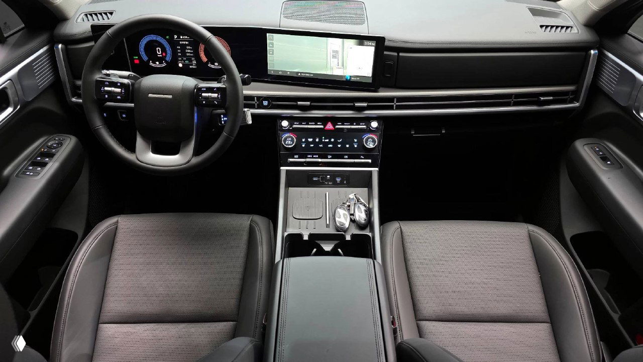 Салон Hyundai Santa Fe 2025, вид на передние сиденья, центральный тоннель, руль и большой широкоформатный экран мультимедиа с ключами в подстаканнике.