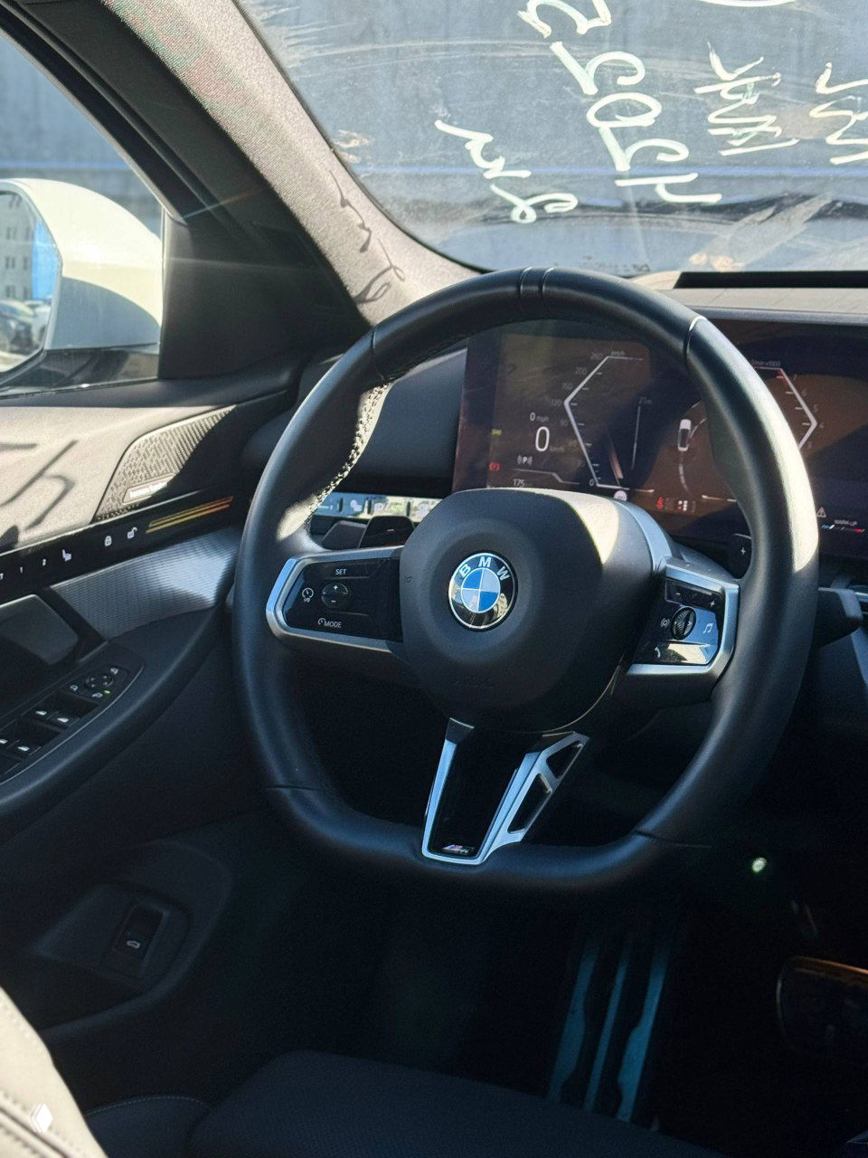 Рулевое колесо BMW с логотипом, часть цифровой приборной панели и отделка двери — вид салона со стороны водителя и верхней частью торпедо.