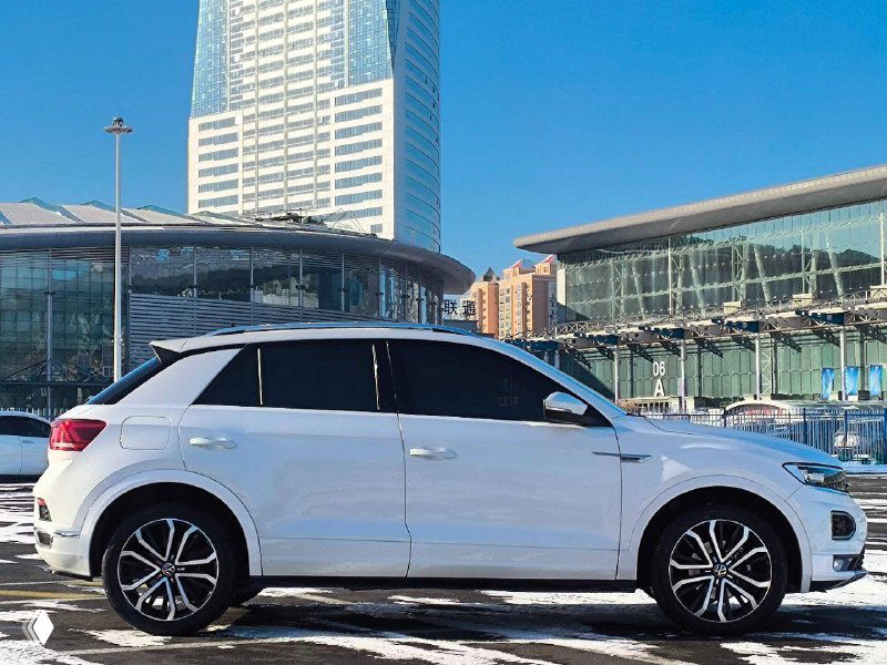 Боковой профиль белого Volkswagen T‑Roc на открытой площадке, подчёркивается форма кузова и диски; демонстрация состояния автомобиля перед отправкой