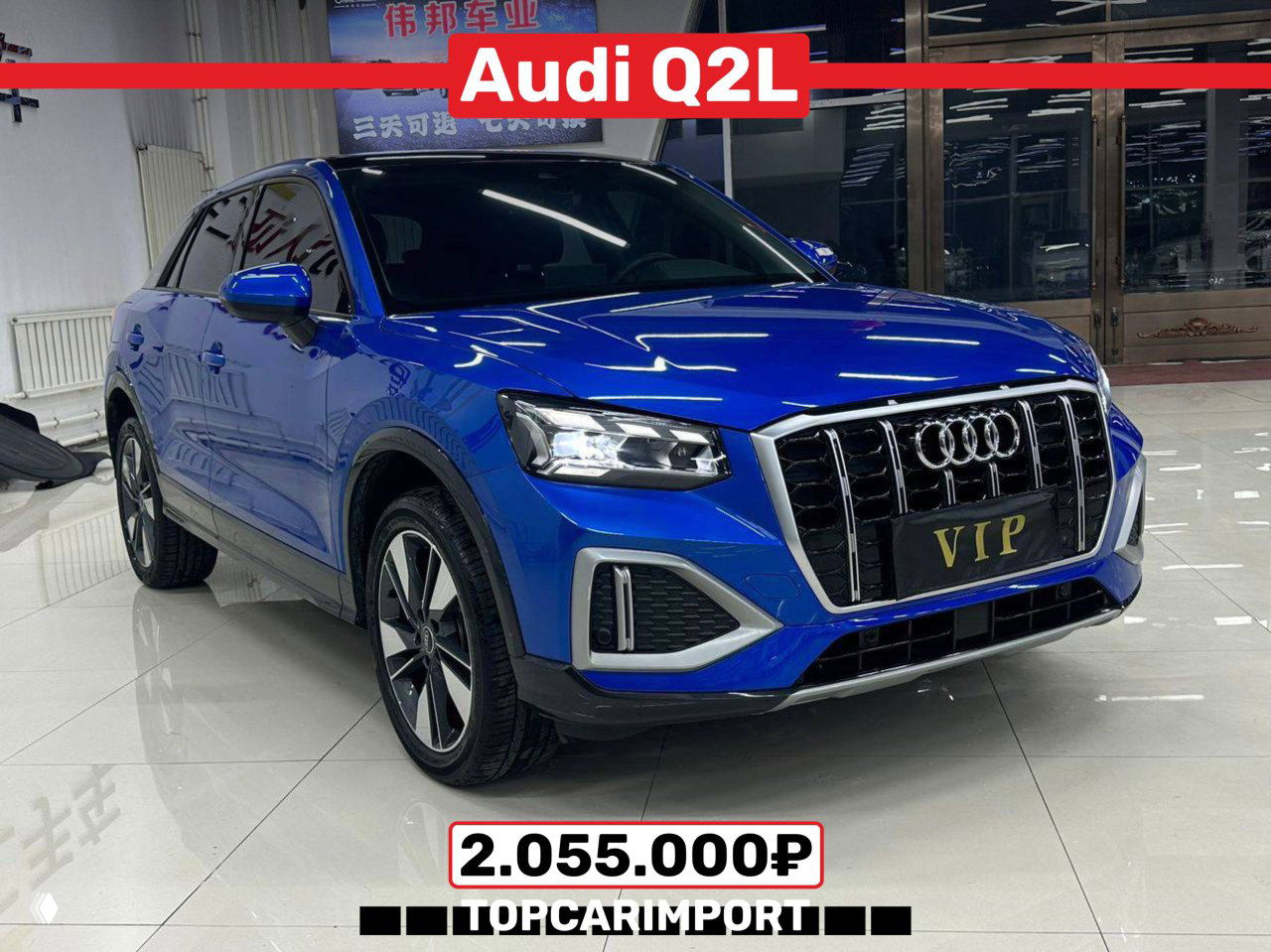 Синий Audi Q2L 2021 года в освещённом шоуруме, вид три четверти; компактный кроссовер с ценой 2.055.000₽ и чистым кузовом.