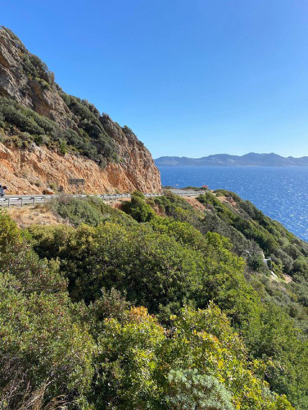 Извилистая прибрежная дорога между скал и кустарников с видом на синее море, типичный пейзаж маршрута из Каша в Калкан.