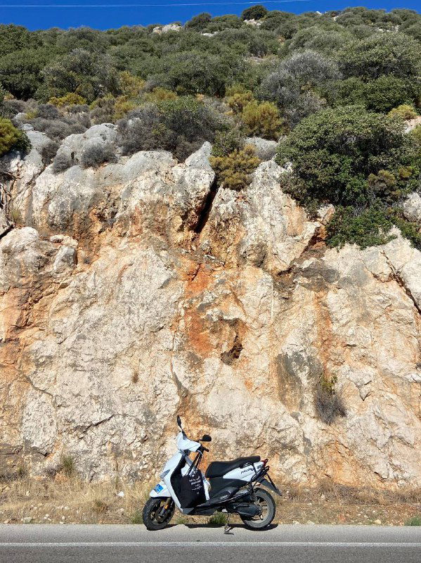 Скутер припаркован у основания каменистого обрыва, на фоне видна сухая растительность и скалистый склон — фото на маршруте вдоль побережья.