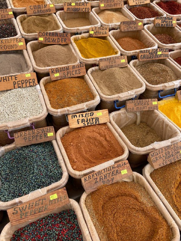 Ряды открытых мешков и коробов со специями и приправами на турецком рынке: паприка, чёрный и белый перец, смеси с табличками и ценниками