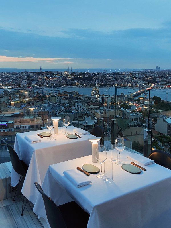 Панорамный вид на Стамбул с высоты: стол на террасе с белой скатертью и широкая панорама города и пролива Босфор на фоне.