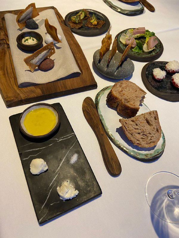 Набор закусок и хлеба на деревянной доске, мелкие порции и элементы авторской подачи в ресторане высокой кухни.