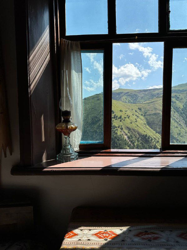 Окно комнаты с видом на горы: свет через стекло, долина внизу и рисунок неба над дагестанскими склонами.