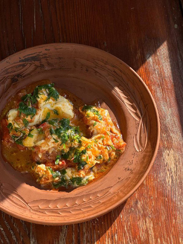 Блюдо аварского чуду в керамической тарелке на деревянном столе, видна зелень, соус и традиционная подача домашней выпечки.