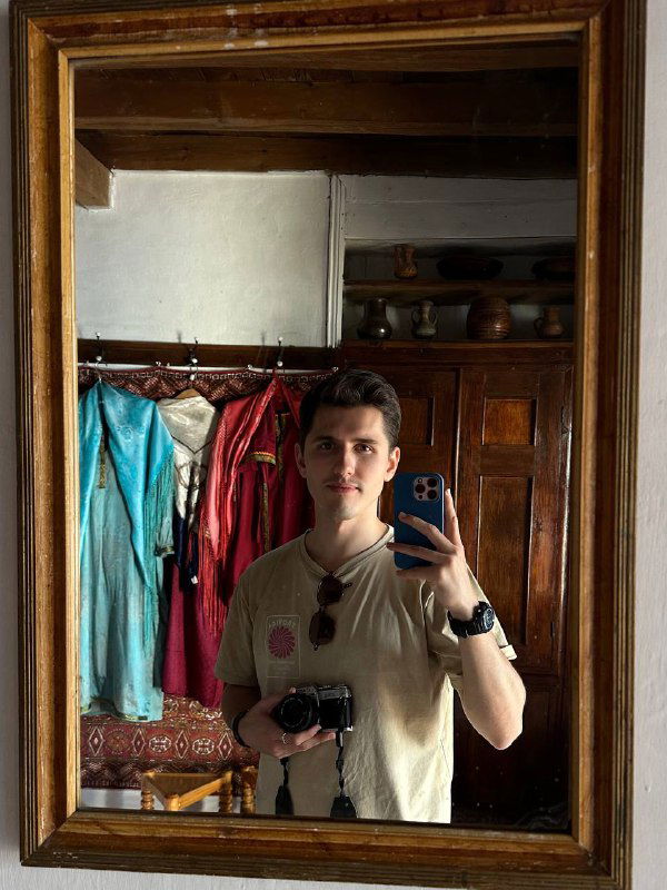 Зеркальное селфи туриста в интерьере сакли с отражением деревянной мебели, традиционных текстильных элементов и посуды.