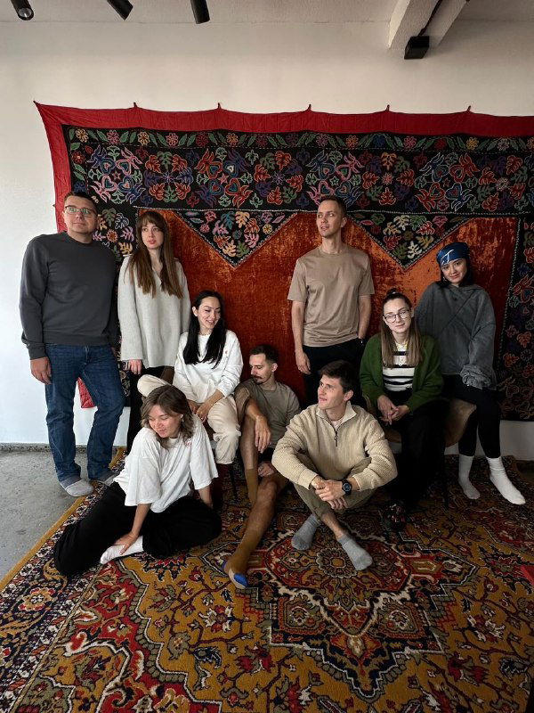 Группа путешественников Tur de Friends в гостеприимном интерьере с национальным ковром и тёплой атмосферой — знакомство с локальной культурой и командой.