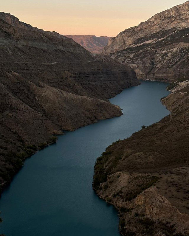 Узкое водохранилище между высокими скалами в Дагестане на закате: сдержанные тёплые тона и спокойная поверхность воды.