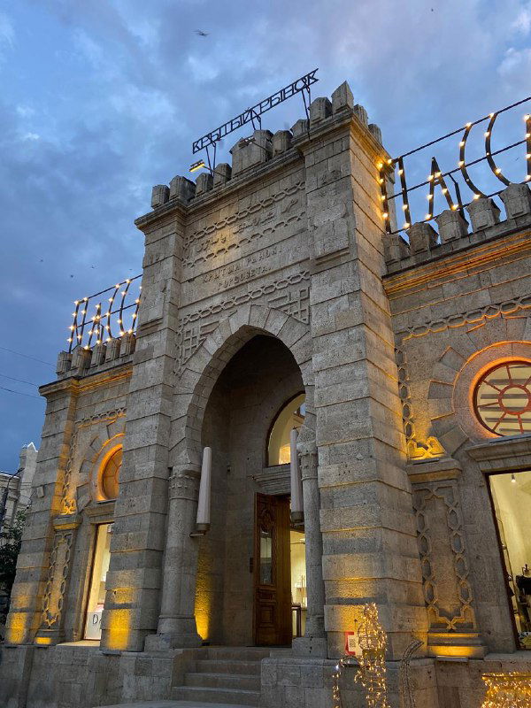 Нарядный фасад здания вокзала или исторической станции в вечерней подсветке на фоне тёмнеющего неба в одном из дагестанских городов.