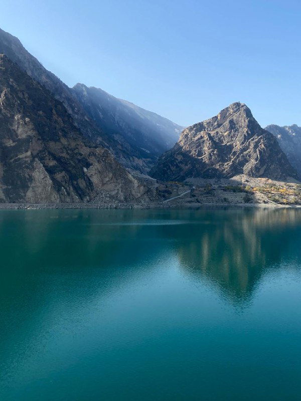 Бирюзовое горное озеро в ясную осеннюю погоду, окружённое крутыми скалами и чистым небом, отражающимся в воде.