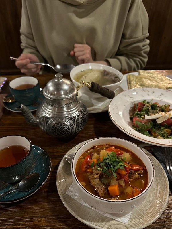 Тарелки с блюдами кавказской кухни и чайник на деревянном столе в тёплом интерьере — еда как часть горного отдыха и местной гастрономии.