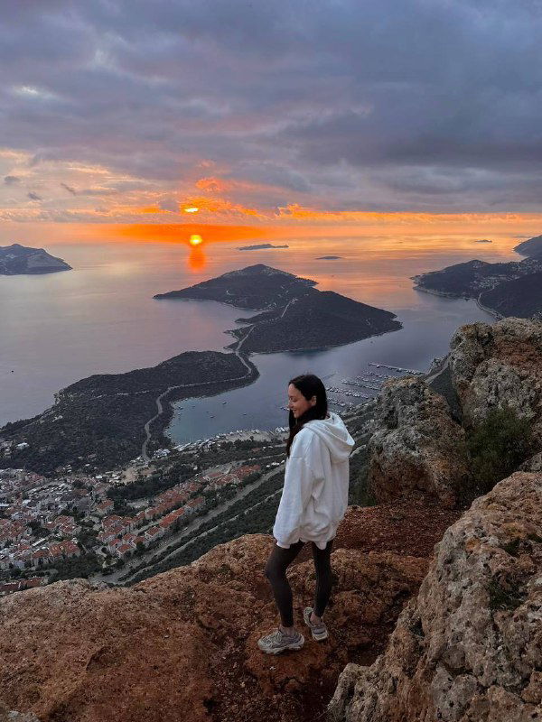 Вид со смотровой площадки на бухту и острова при ярком восходе/закате; человек на переднем плане добавляет масштаба пейзажу.