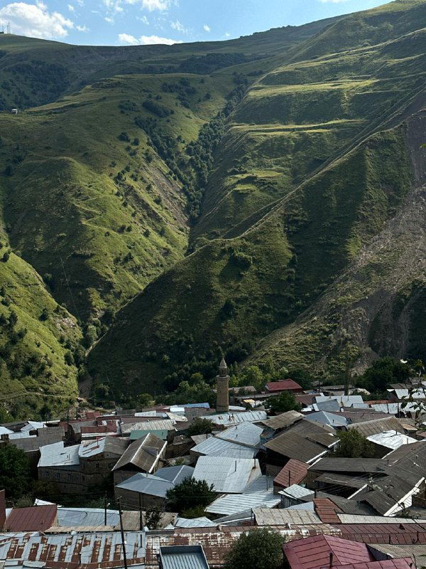 Панорама горного ущелья и крыши аульских домов на фоне зелёных склонов — пейзаж Дагестана и уклад жизни в горах.