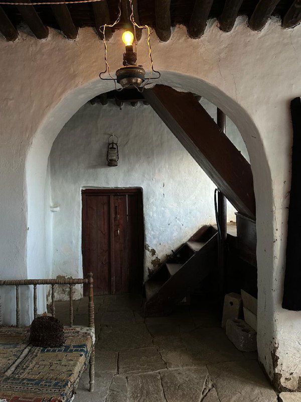 Интерьер старого дома/кофейни: арочные белые стены, деревянная балка, винтажная лампа и коридор со лестницей.