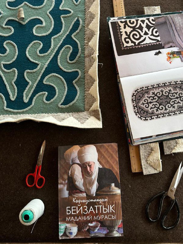 Рабочее место: куски текстиля, книги по орнаментам и инструменты для обработки шерсти и изготовления ковров и ремесленных изделий.