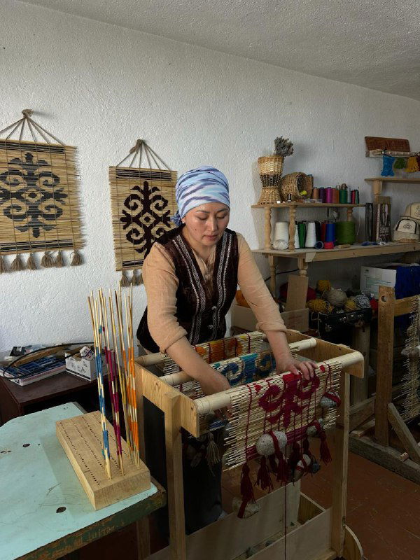 Женщина за ткацким станком вплетает нити в ковер в мастерской — традиционная техника и сосредоточенная работа рук мастерицы.